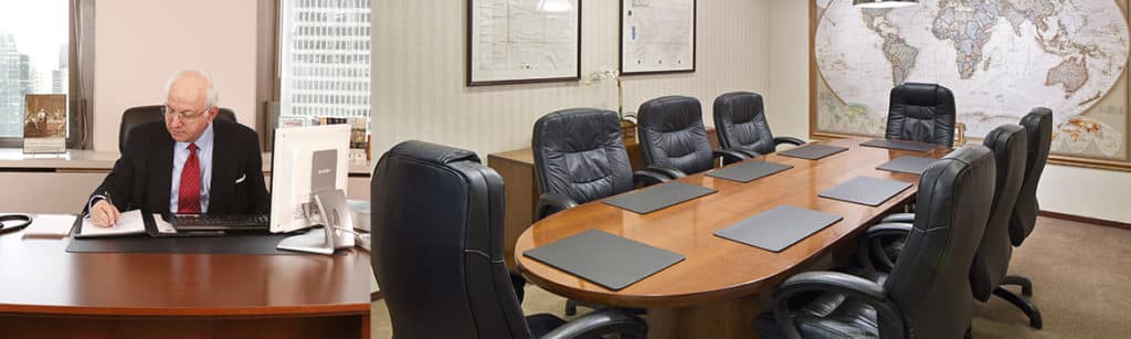 An older man sits at a desk in an office setting, writing on a paper. Adjacent is a conference room with a long table, eight chairs, and a large world map on the wall.