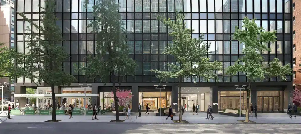Street view of a modern building with a glass facade, trees lining the sidewalk, and people walking.