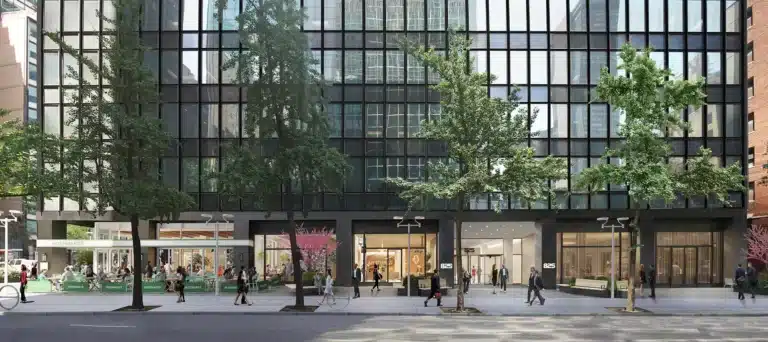 Street view of a modern building with a glass facade, trees lining the sidewalk, and people walking.