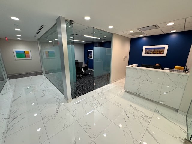 Modern office lobby with white marble floor, a reception desk, glass-walled conference room, and framed artwork on blue and white walls.