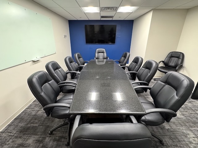 A modern conference room with a long black table, ten black leather chairs, a wall-mounted TV, and a whiteboard.