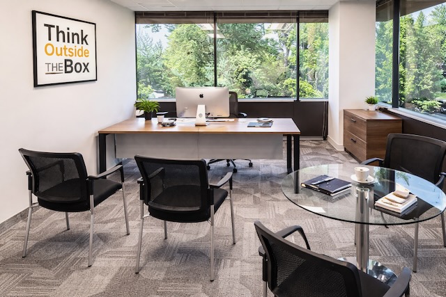 Modern office with a large desk, three chairs, a computer, and a "Think Outside the Box" sign on the wall.