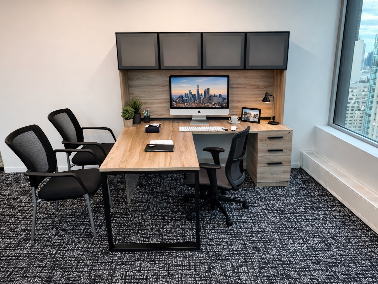 Modern office with a wooden desk, computer, three chairs, and a city view through a large window.