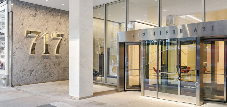 Entrance to a modern building with "717" displayed on the wall and "717 Fifth Ave" above glass doors.