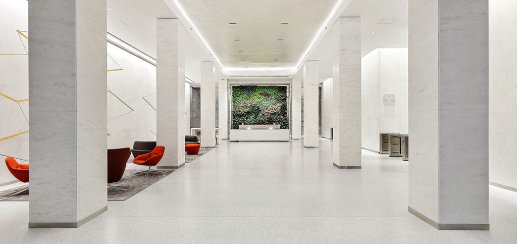 Spacious modern lobby with white marble columns, red chairs, and a green living wall at the far end.