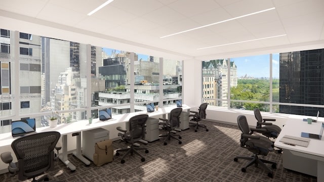Modern office with desks and chairs by large windows overlooking city buildings and a park.