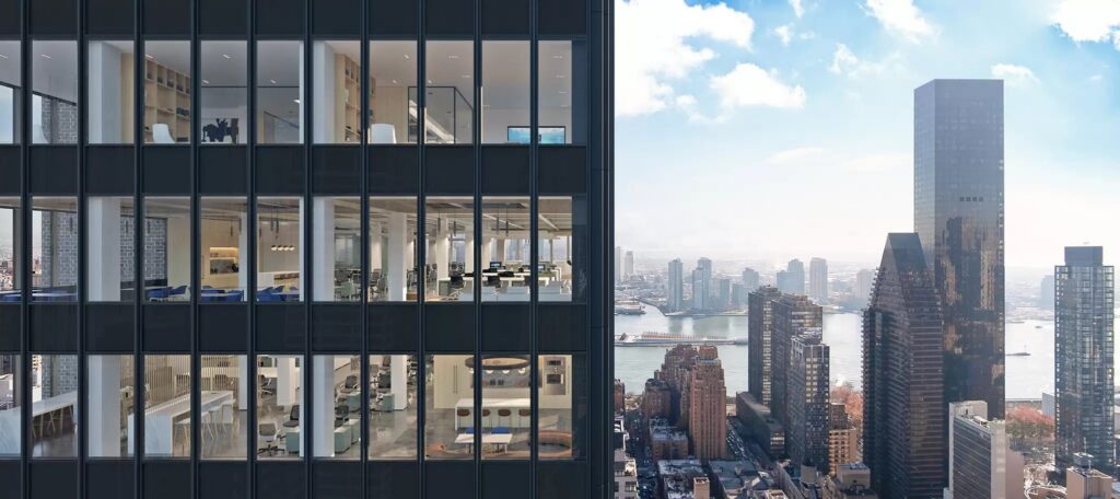 Modern office building with large glass windows overlooking a city skyline and river on a bright day.