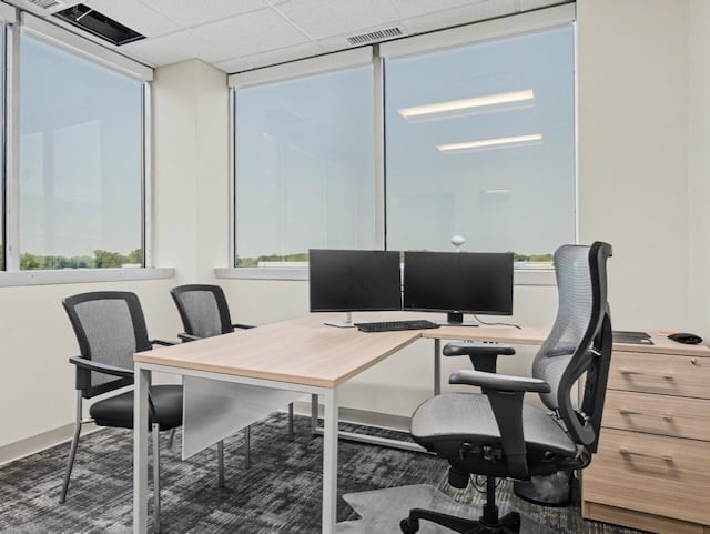 Modern office with three chairs, a desk, two monitors, and large windows with a view outside.