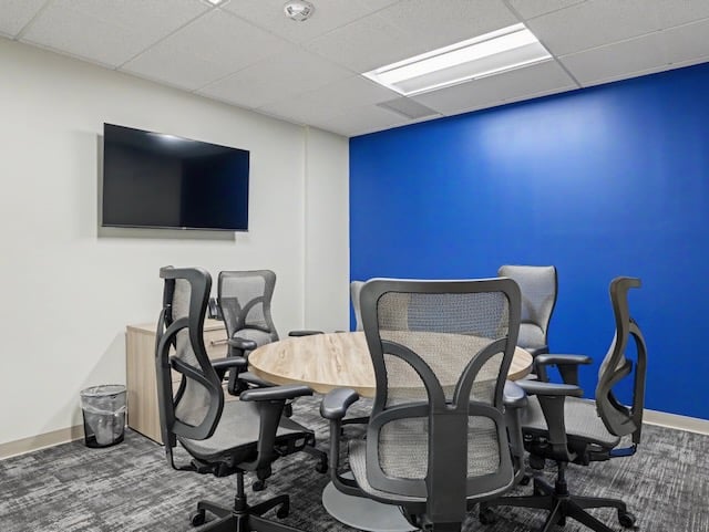 Small meeting room with five mesh chairs around a round table, blue accent wall, and wall-mounted TV.