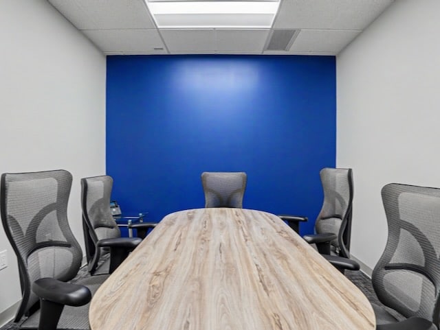 Small conference room with a wood table, five gray chairs, and a vivid blue accent wall.