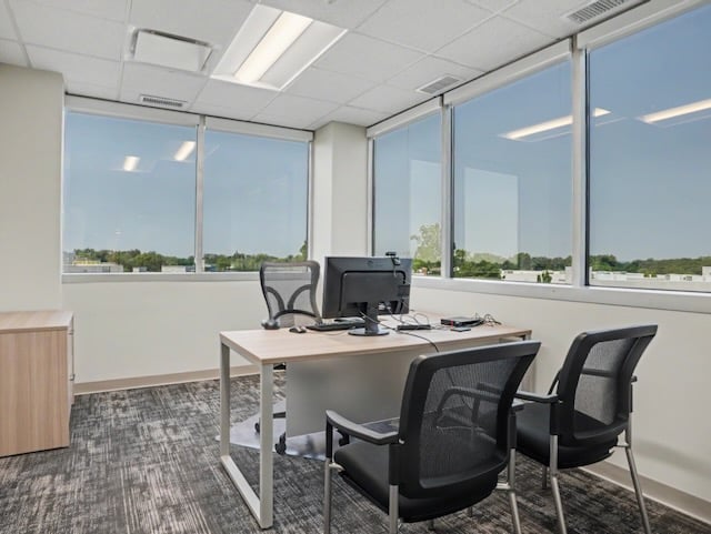 Modern office with two chairs, a desk, and a computer by large windows overlooking trees and buildings.