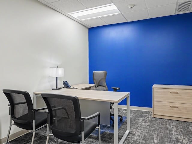 Modern office with a desk, three chairs, lamp, phone, and a blue accent wall.