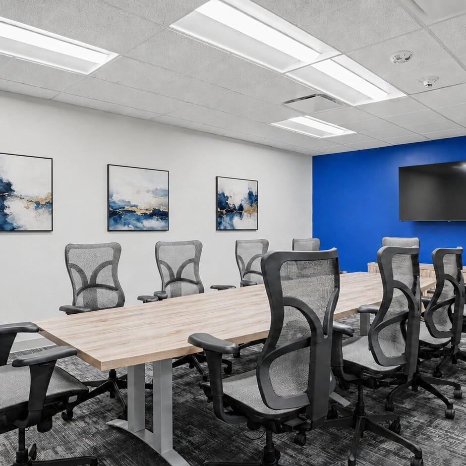 Modern conference room with mesh chairs, a large table, blue accent wall, and abstract art on the wall.