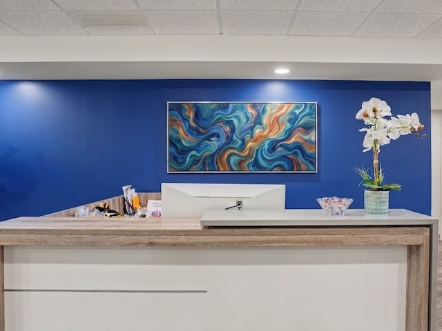 Reception desk with a vase of orchids, blue accent wall, and colorful abstract painting above.
