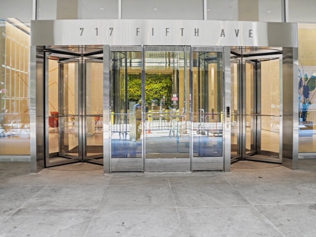 Revolving glass doors at the entrance of a building labeled “717 Fifth Ave” with reflections visible.