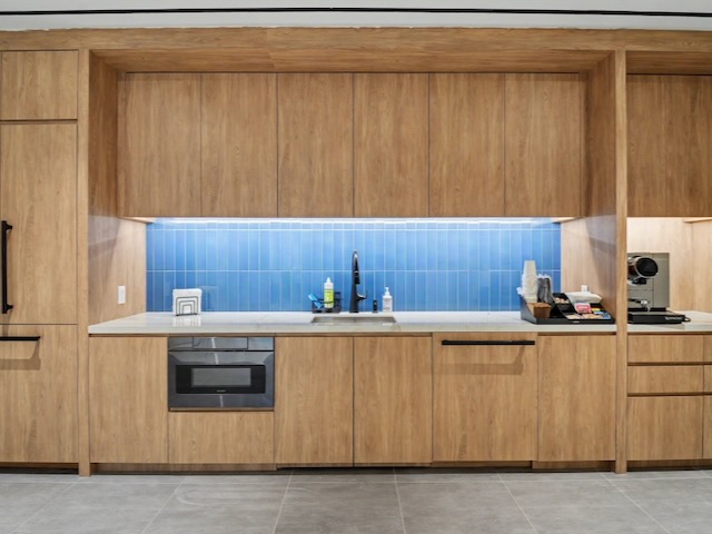 Modern kitchen with wood cabinets, a sink, blue tile backsplash, and gray floor tiles.