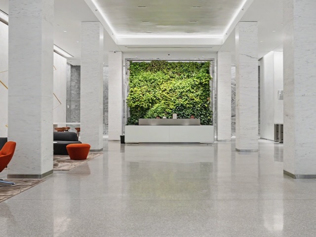 Modern lobby with white walls, a green plant wall behind the reception desk, and orange chairs on the left.