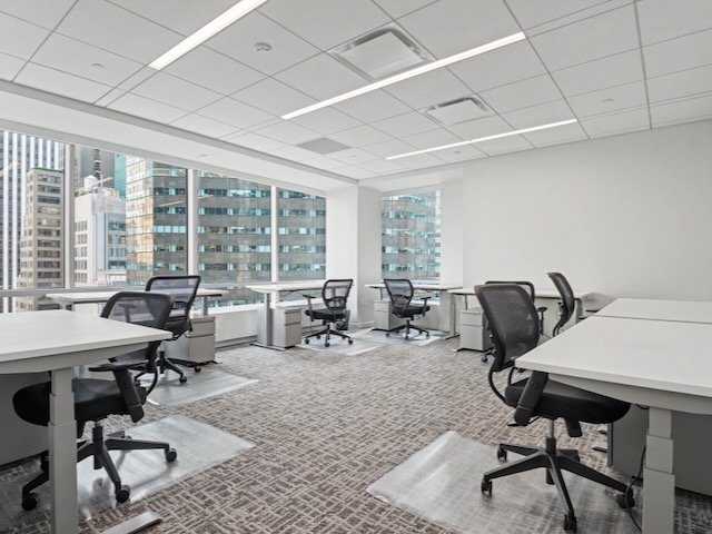 Modern office with empty desks and chairs, large windows, and city buildings visible outside.
