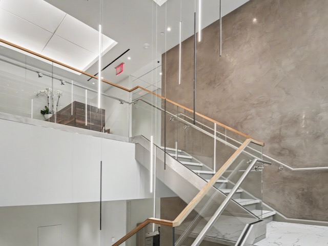 Modern staircase with glass railings, wood accents, pendant lights, and a marble-patterned floor.