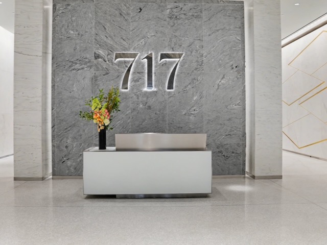 Modern lobby with “717” on a gray stone wall behind a sleek white reception desk with a flower arrangement.