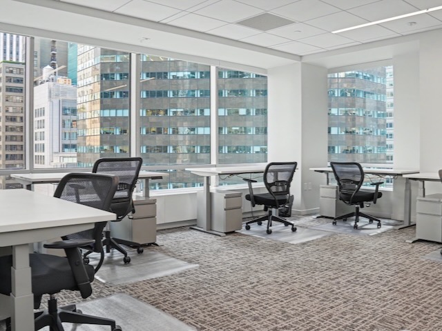 Modern office with empty desks and chairs, large windows, and city buildings visible outside.