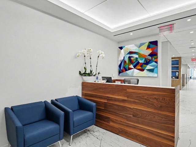 Modern office lobby with blue chairs, wood reception desk, orchid, and colorful abstract wall art.