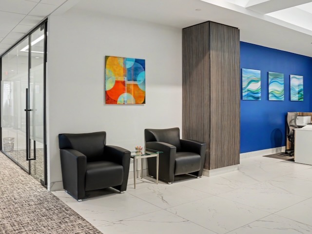 Modern office waiting area with two black chairs, small table, and colorful abstract art on the walls.