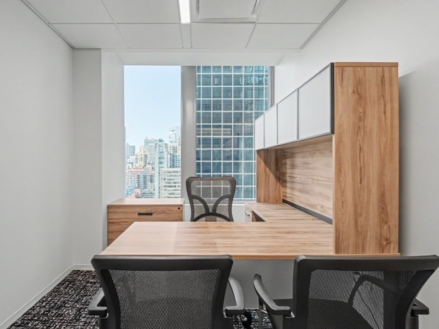 Modern office with wood desk, two chairs, large window showing city skyscrapers, and white walls.