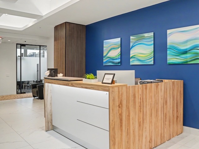 Reception desk with wood accents, blue wall, three abstract paintings, and modern office decor.