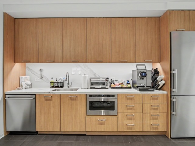 A modern kitchen with wood cabinets, stainless appliances, a sink, and a coffee machine on the countertop.