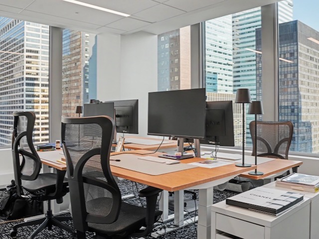 Modern office with four chairs, computers on desks, large windows, and city buildings outside.