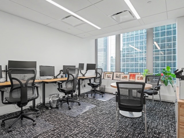 Modern office with desks, chairs, computers, large windows, and framed pictures on the windowsill.
