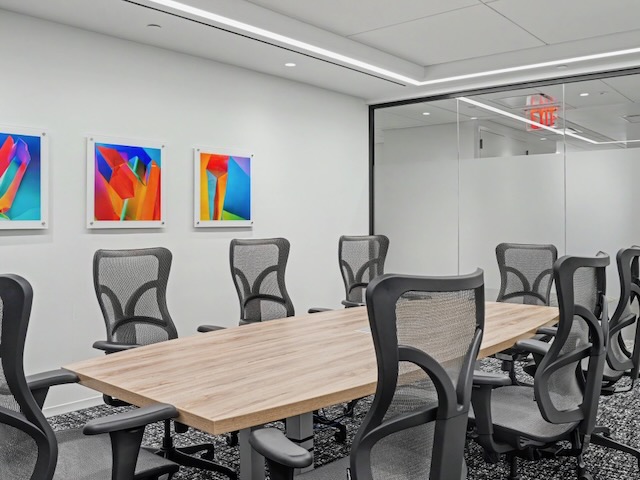 Modern conference room with mesh chairs, wooden table, white walls, and colorful abstract art on the wall.