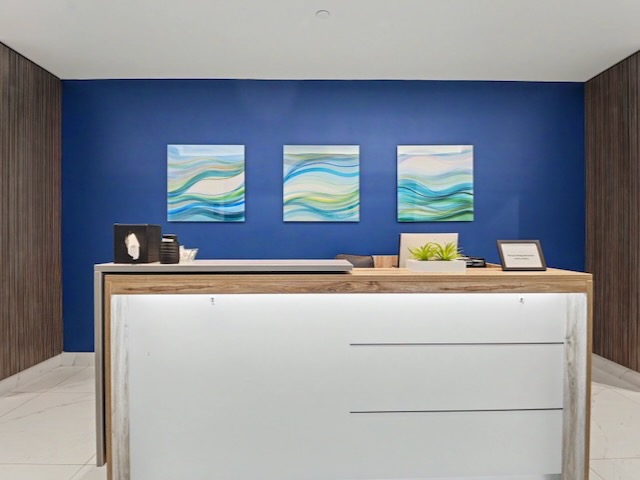 Modern reception desk with decor in front of a blue wall featuring three abstract wave paintings.