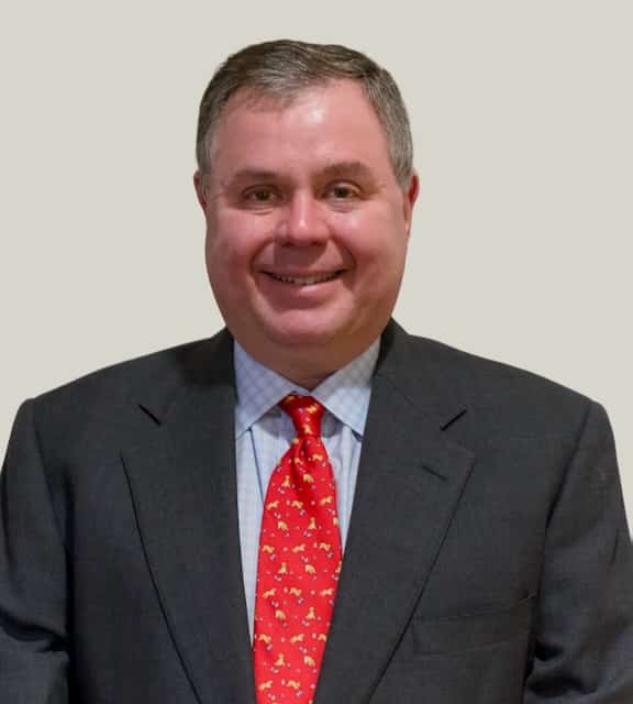 Man in a dark suit and red patterned tie smiling in front of a plain light background, embodying the professional atmosphere often found in an executive office or Westchester NY virtual office.