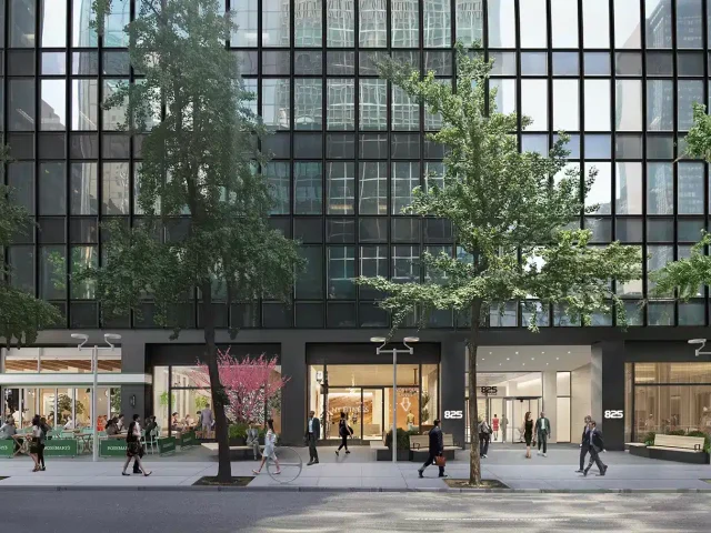 Street view of a modern building with a glass facade, trees lining the sidewalk, and people walking.