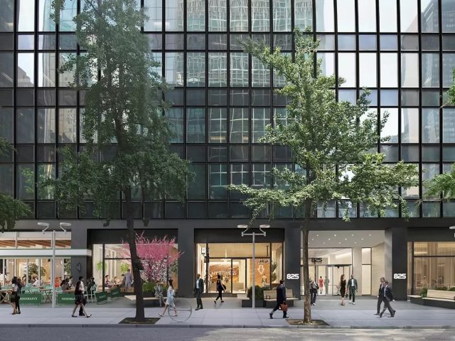 Street view of a modern glass building with trees and people walking on the sidewalk.