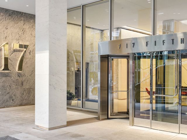 Entrance to a modern building with "717" displayed on the wall and "717 Fifth Ave" above glass doors.
