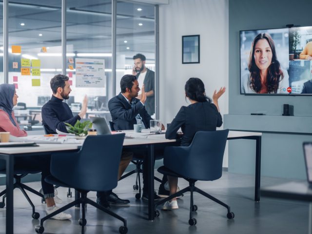 Businesspeople do Video Conference Call with Big Wall TV in Office Meeting Room. Diverse Team of Creative Entrepreneurs at Big Table have Discussion. Specialists work in Digital e-Commerce Startup